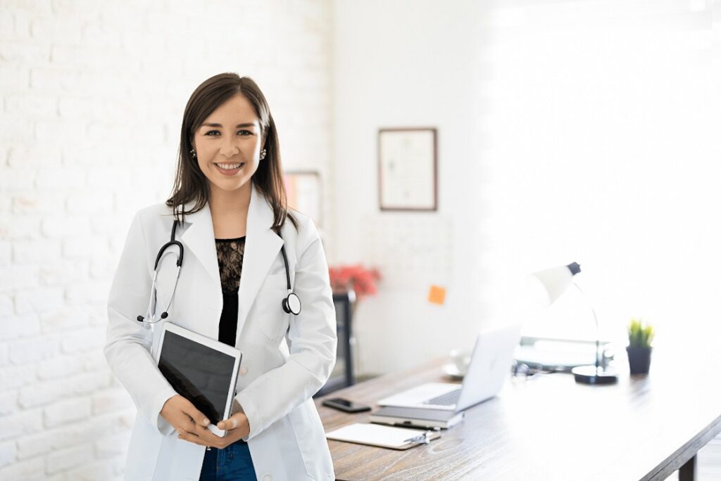 An Asian female doctor confidently holds a tablet in her modern office while reviewing MCC Objectives for MCCQE1 Qbank.