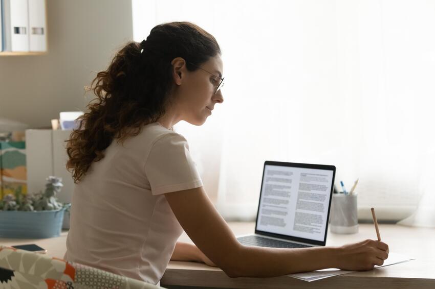 A woman working on her laptop at home, preparing for the MCCQE1 exam.