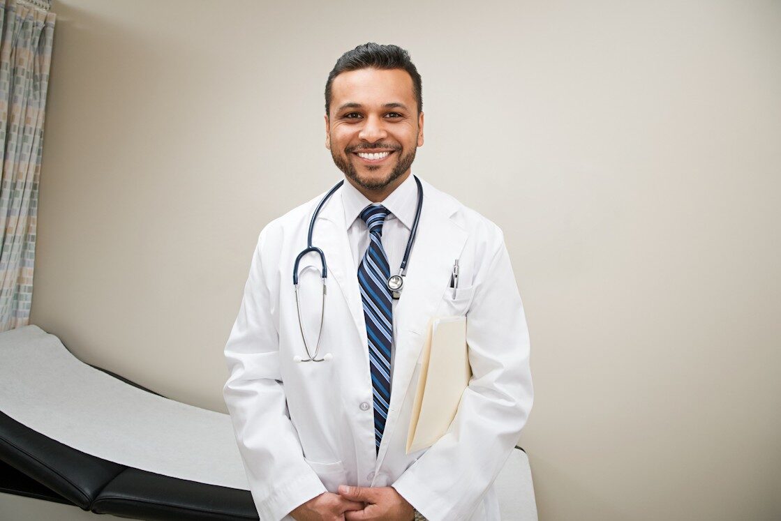A male doctor standing in front of a bed speaking about the final review for MCCQE1.