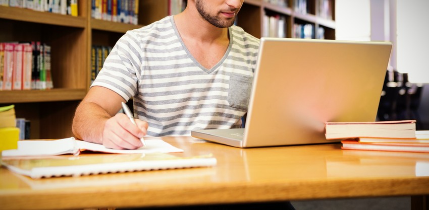 A man working on a laptop in a library for MCCQE1 exam preparation.