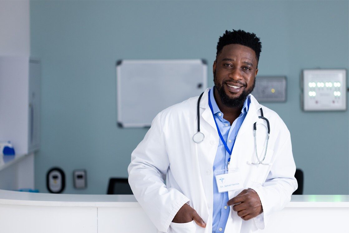 A black male doctor standing in front of a reception desk, passed the MCCQE1 exam.