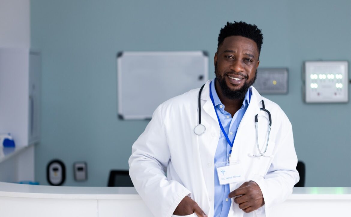 A black male doctor standing in front of a reception desk, passed the MCCQE1 exam.