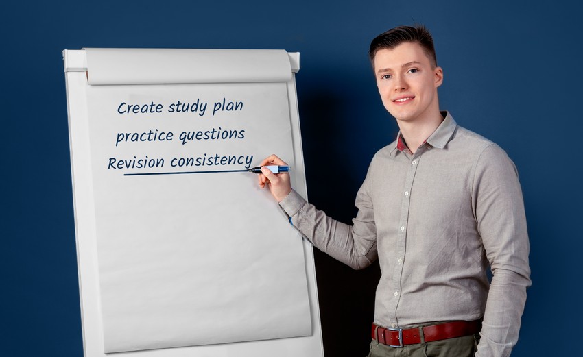 Young medical student in a grey shirt writing a study plan for MCCQE1 on a flip chart with a blue background.