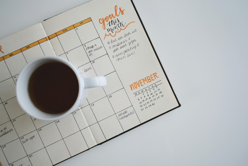 A cup of coffee placed next to an open planner with goals written for the month of November, including MCCQE1 exam preparation.