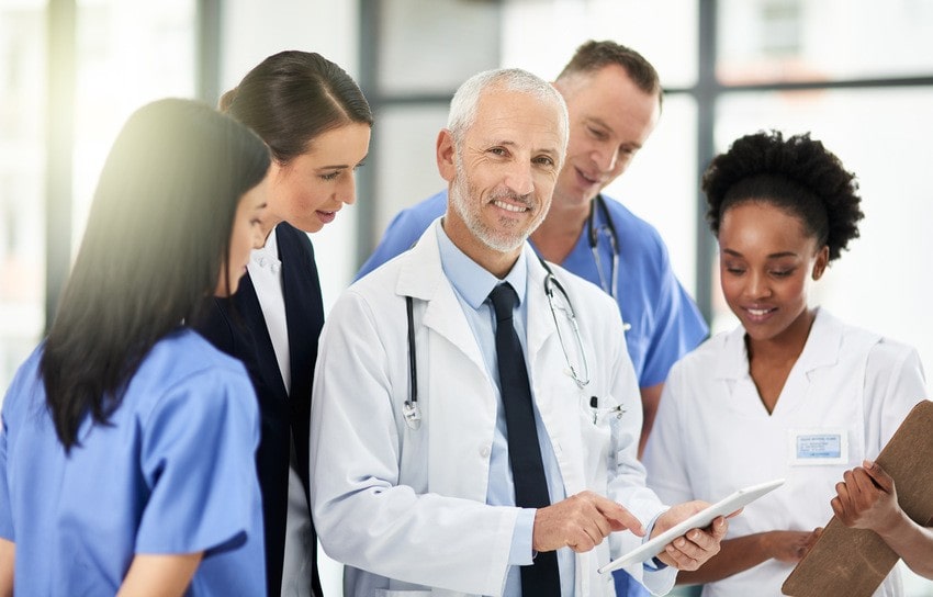 A group of healthcare professionals, including doctors and nurses, stand together in a hospital setting, reviewing Medicine in Canada resources on a digital tablet as part of their MCCQE1 exam Prep.
