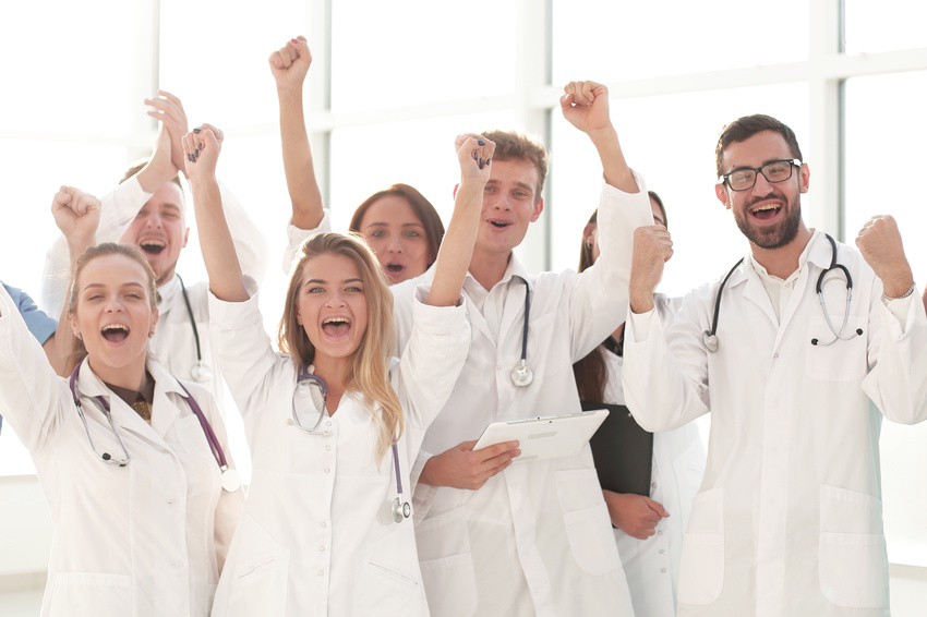 A group of doctors in white coats stand together, smiling and raising their fists in celebration, inspired by the latest MCCQE1 Qbank New Update that empowers Canadian medicine.