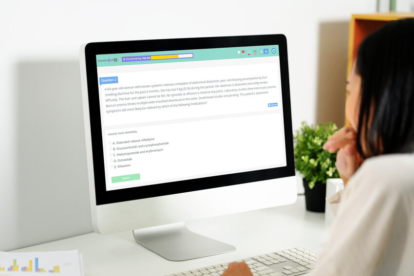 A person sits at a desk using a desktop computer to answer a multiple-choice question on Ace QBank for the MCCQE1 exam preparation.