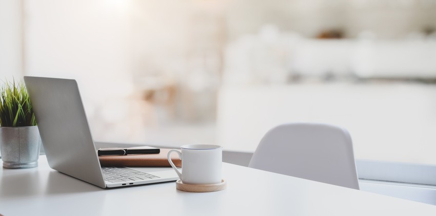 A laptop, a notebook, a pen, a potted plant, and a white coffee mug on a white desk in a bright, modern workspace. Perfect for exploring the Ace QBank new update with more questions for better MCCQE1 exam prep.