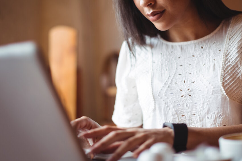 A woman wearing a white embroidered blouse types on a laptop, possibly preparing for her MCCQE1 exam with Ace QBank. Her last chance to secure your MCCQE Part 1 pass in 2025. Only her hands and partial face are visible.
