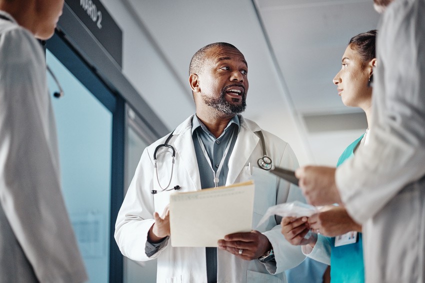 A doctor holding a file speaks with medical staff in a hospital corridor, discussing Ace QBank resources for MCCQE1 exam preparation.