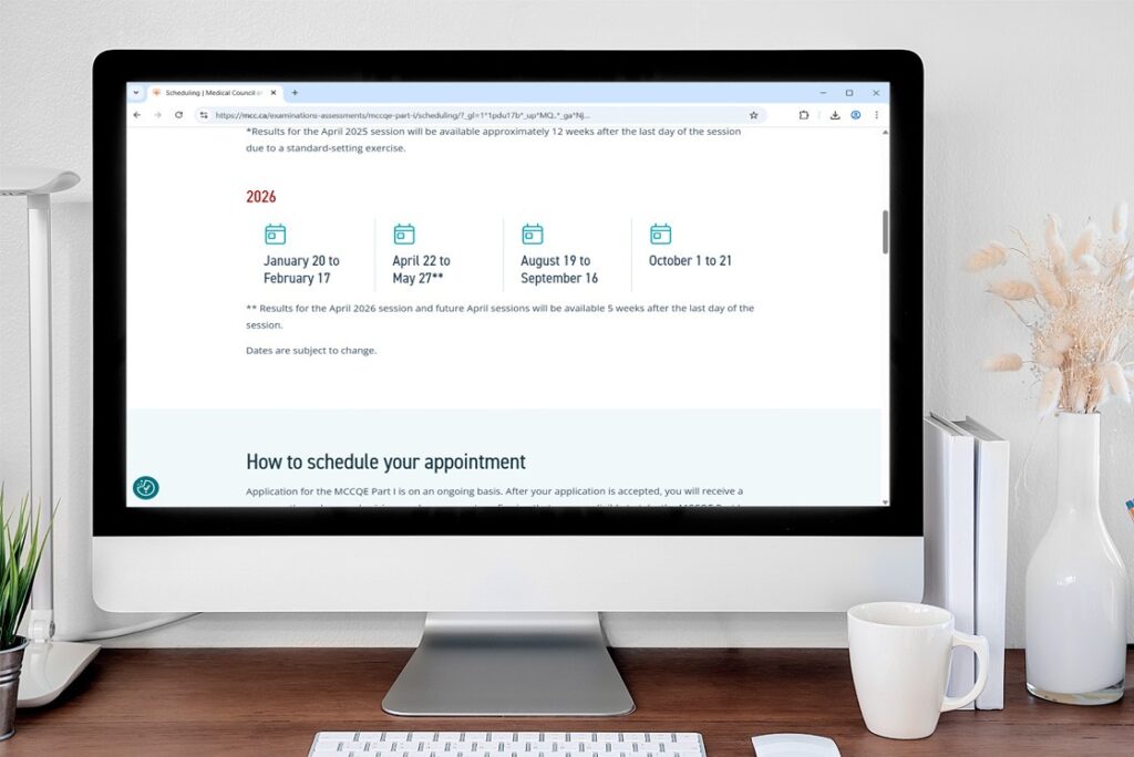 A computer monitor displays a scheduling webpage with 2026 MCCQE Part 1 Exam Dates and session details. A keyboard, mouse, and vase with dried flowers are on the white desk. Ideal for focused MCCQE1 Exam Preparation with Ace QBank.
