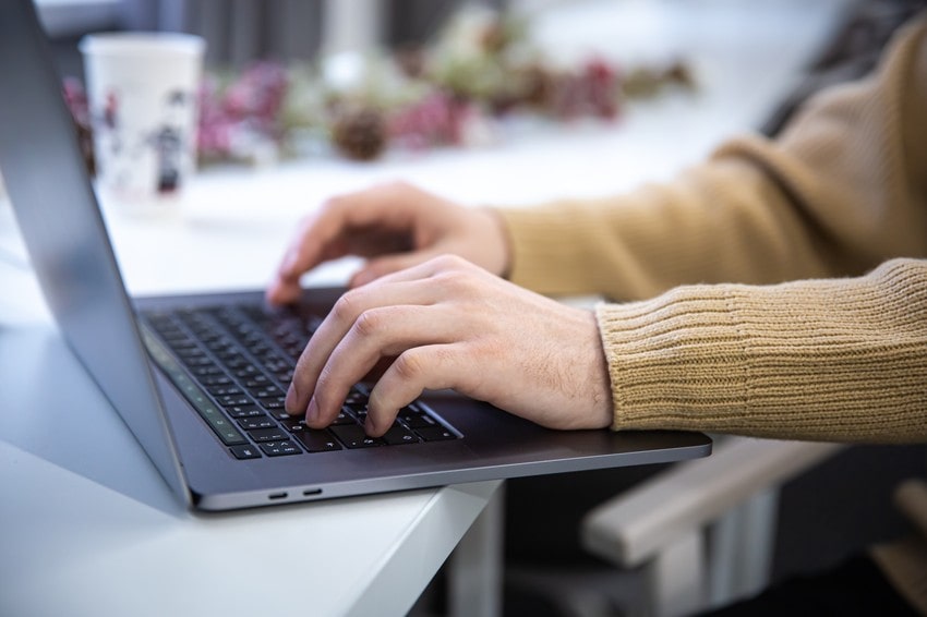 Close-up of a person in a tan sweater typing on a laptop at a desk, with a cup and blurred decorations in the background. Perfect for MCCQE1 exam preparation or trying free Ace QBank demo questions.