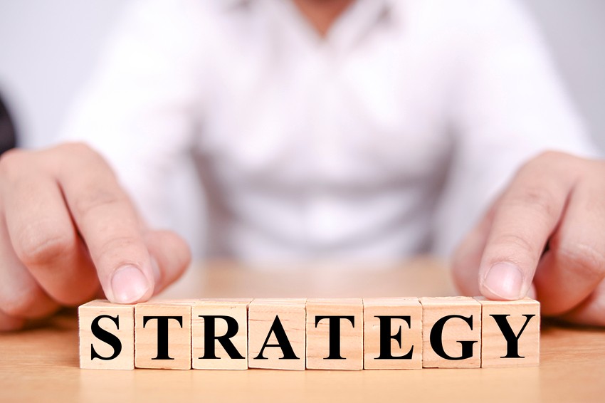 A person in a white shirt arranges wooden blocks on a table to spell out "STRATEGY," symbolizing focused MCCQE1 exam preparation with Ace QBank.