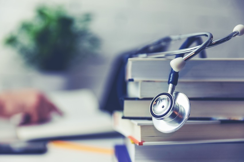 A stethoscope rests on a stack of textbooks, with a blurred hand turning a page in the background. A scene familiar to anyone focused on MCCQE1 exam preparation.