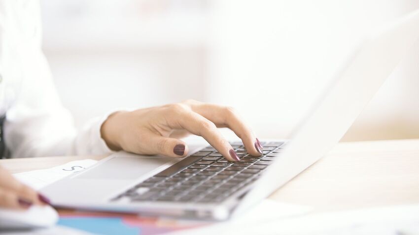 A person’s hand types on a laptop keyboard with documents partially visible on the desk, researching Ace QBank to better understand what MCCQE1 actually demands in 2026.