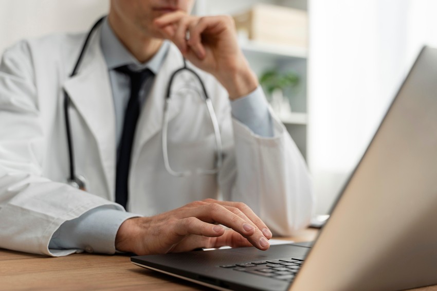 Person wearing a white coat and stethoscope sits at a desk, focused on MCCQE1 exam preparation while looking at a Ace QBank website with one hand on the keyboard.