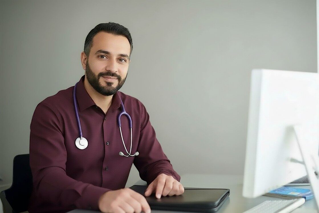 A bearded man wearing a stethoscope sits confidently, looking toward the camera. Ready to discuss the MCCQE1 exam result and validity using Ace QBank.