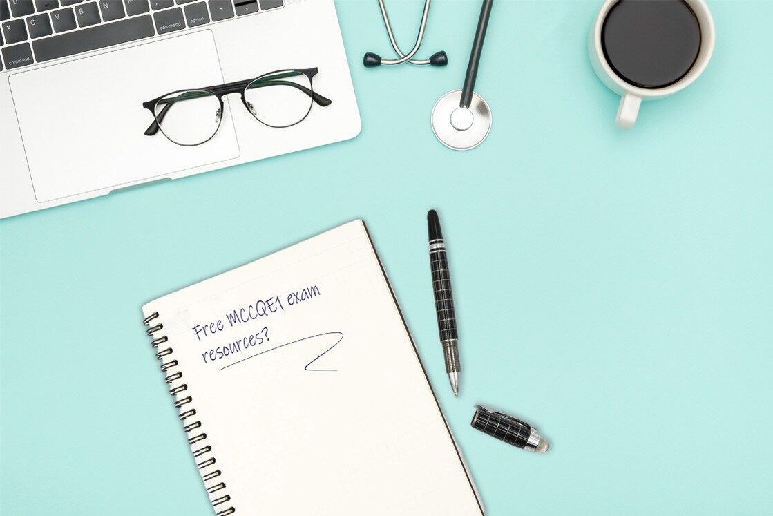 A notebook with "Free MCCQE1 exam resources?" written on it, placed on a desk with Ace QBank materials, pen, glasses, laptop, stethoscope, and a coffee cup. Perfect for your MCCQE1 exam preparation.