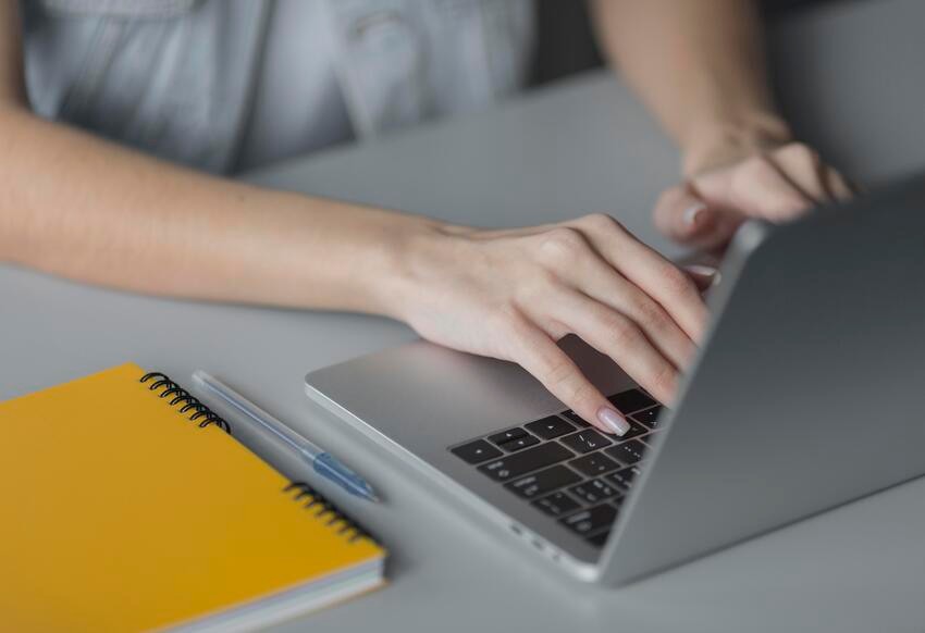 A person types on a laptop at a desk with a yellow notebook and pen nearby, focused on MCCQE1 Exam Preparation and exploring the latest Ace QBank Update 2026 | MCCQE1 Resource.