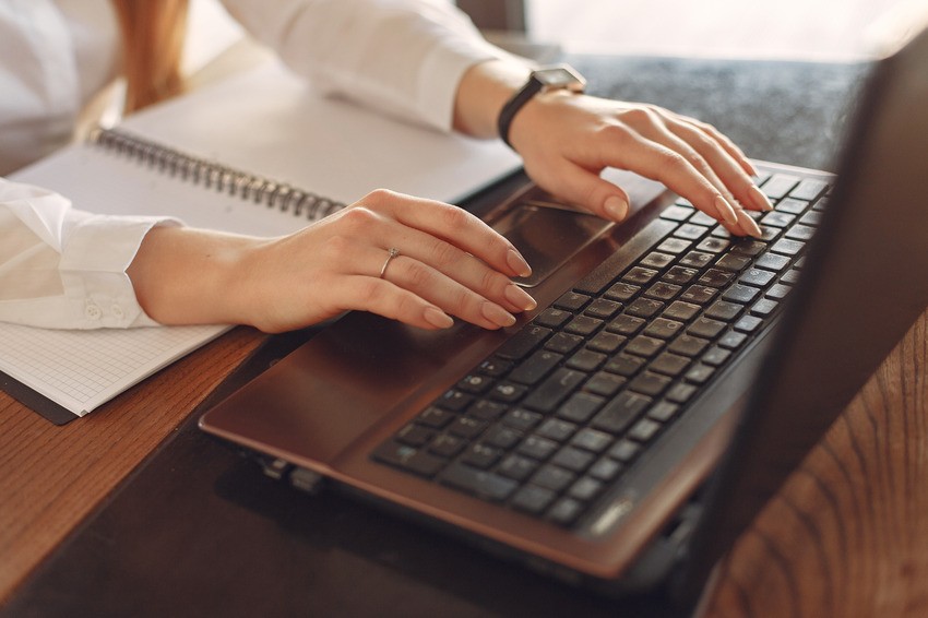 A person types on a laptop keyboard with a notebook nearby on a wooden desk, focused on MCCQE1 exam preparation and discovering what top candidates do differently with Ace QBank.