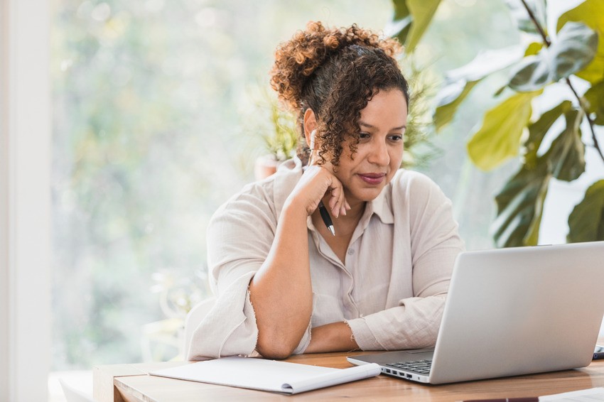 A woman sits at a desk, looking at an Ace QBank MCCQE1 screen with a notebook and pen beside her, in a bright room with plants in the background, reflecting on what top candidates do differently.