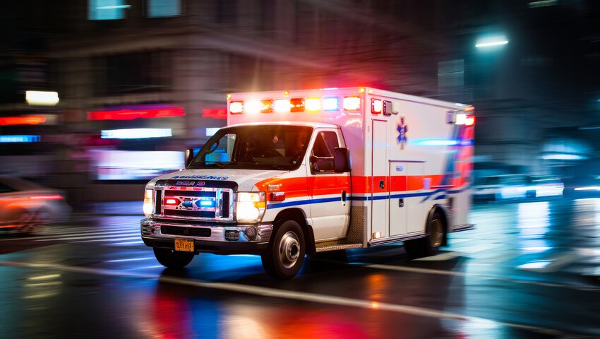 Emergency ambulance with flashing lights speeding through a city street at night, representing a Lyme disease emergency.
